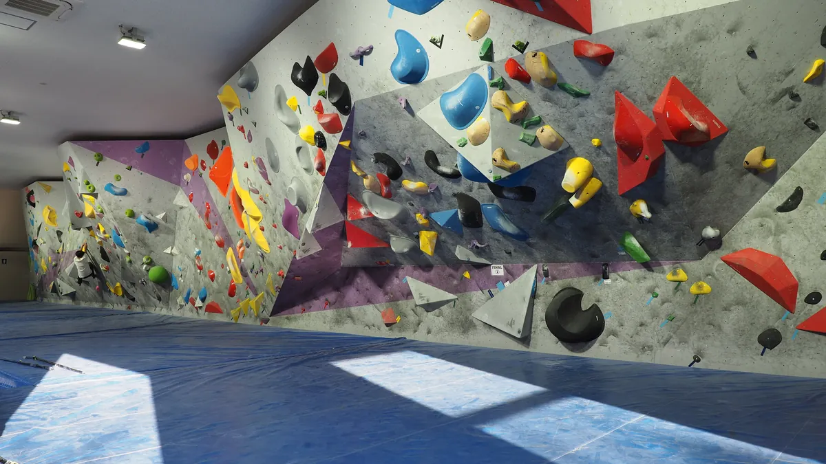 An empty indoor bouldering wall with colourful holds above a blue padded floor